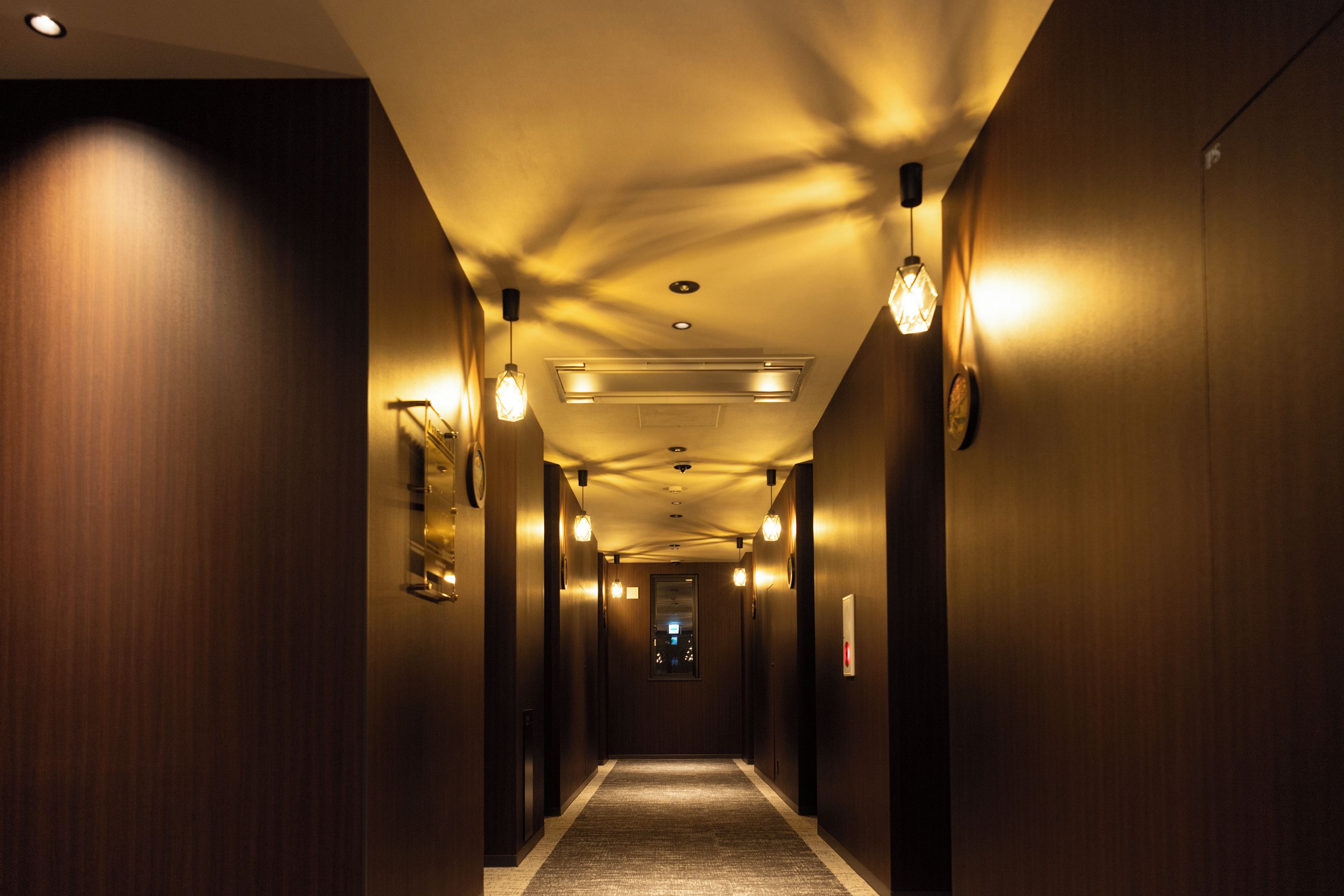 A hotel hallway with wooden walls, recessed lighting, and a carpeted floor.