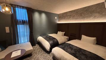 A hotel room with two beds, a small table, and a window with curtains.
