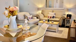 A modern living room with a sofa, coffee table, and a glass dining table with chairs. - Seaside Luxury Cottage *Aldeburgh* (Aldeburgh)