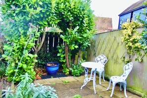 A garden with a table and chairs, a blue pot, and a wooden fence. - Seaside Luxury Cottage *Aldeburgh* (Aldeburgh)