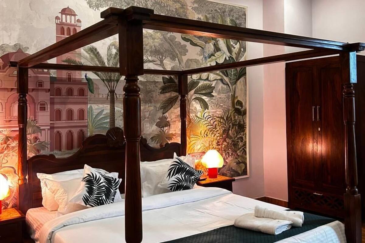 A four-poster bed with a canopy, a nightstand with a lamp, and a mural on the wall.