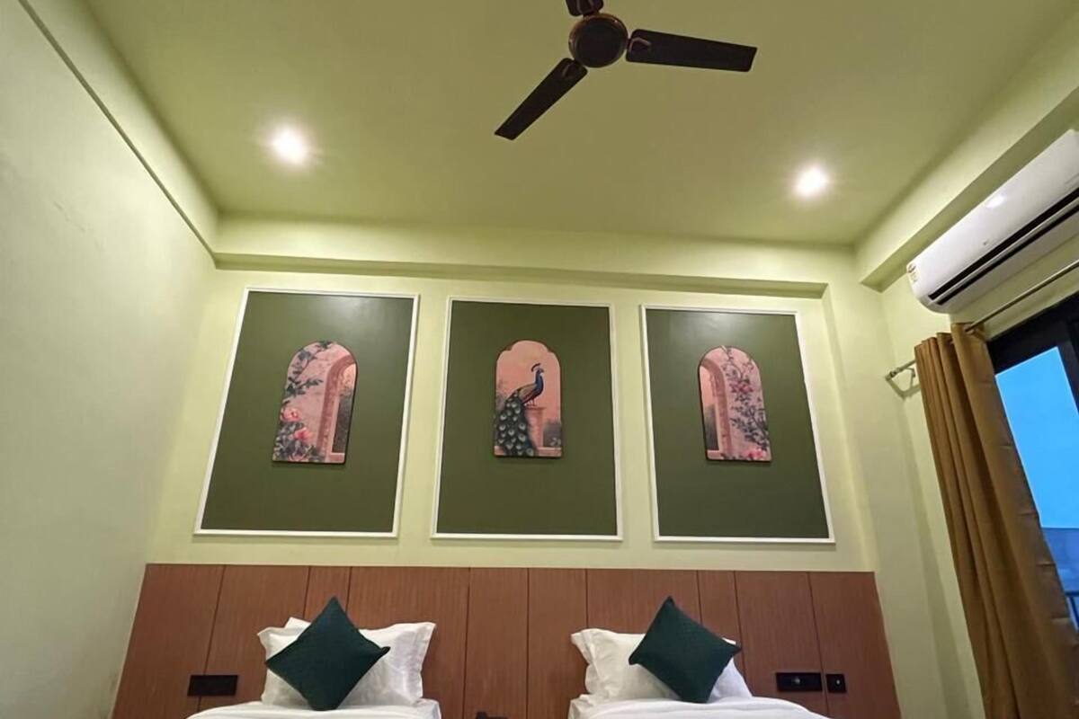 A hotel room with two single beds, a ceiling fan, and three wall-mounted artwork pieces.
