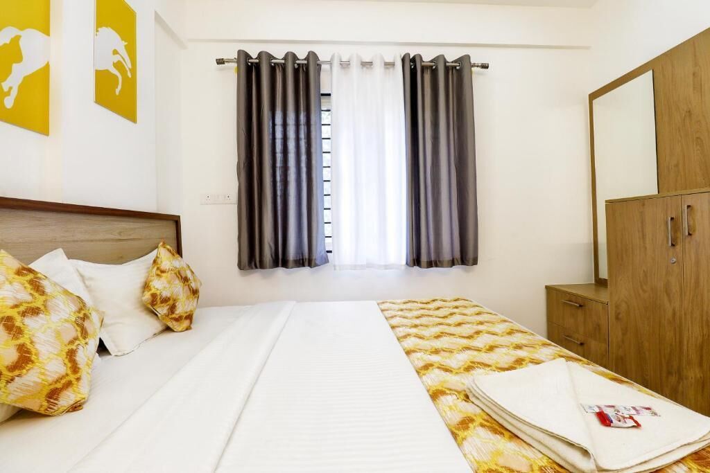 A hotel room with a bed, a wooden wardrobe, and a window with curtains.