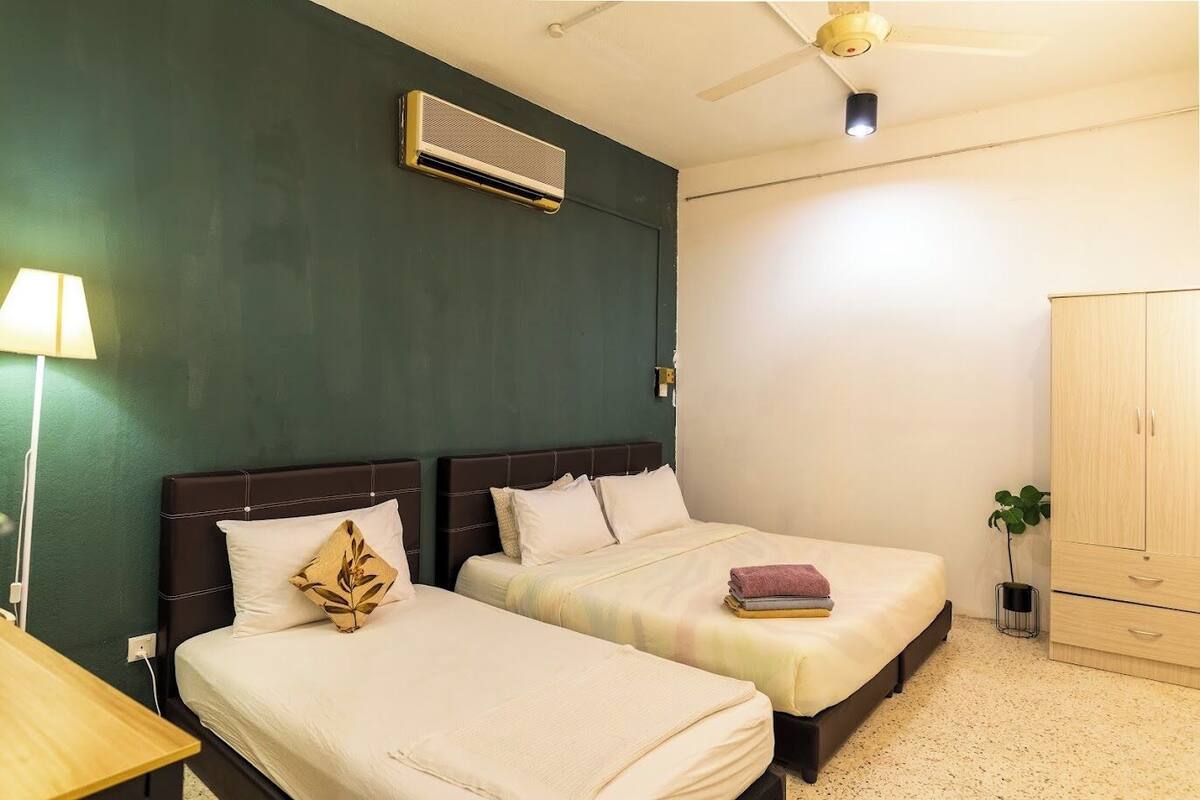 A room with two beds, a ceiling fan, an air conditioning unit, a lamp, a wardrobe, and a small plant.