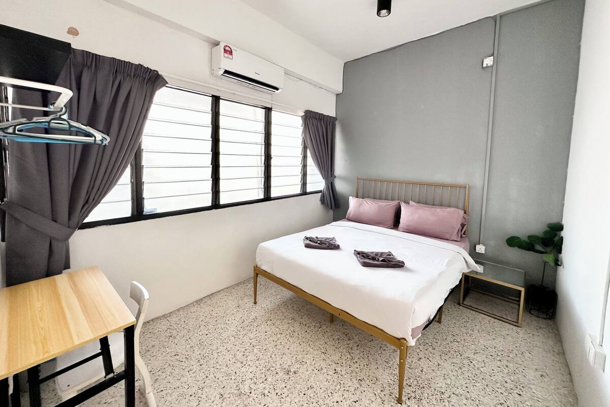 A bedroom with a bed, a desk, a chair, and a window with curtains.