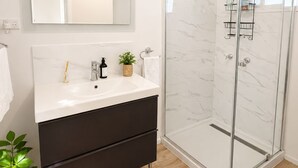 Ein modernes Badezimmer mit Duschkabine aus Glas, einem weißen Waschtisch mit Spiegel und einem dunklen Schrank.