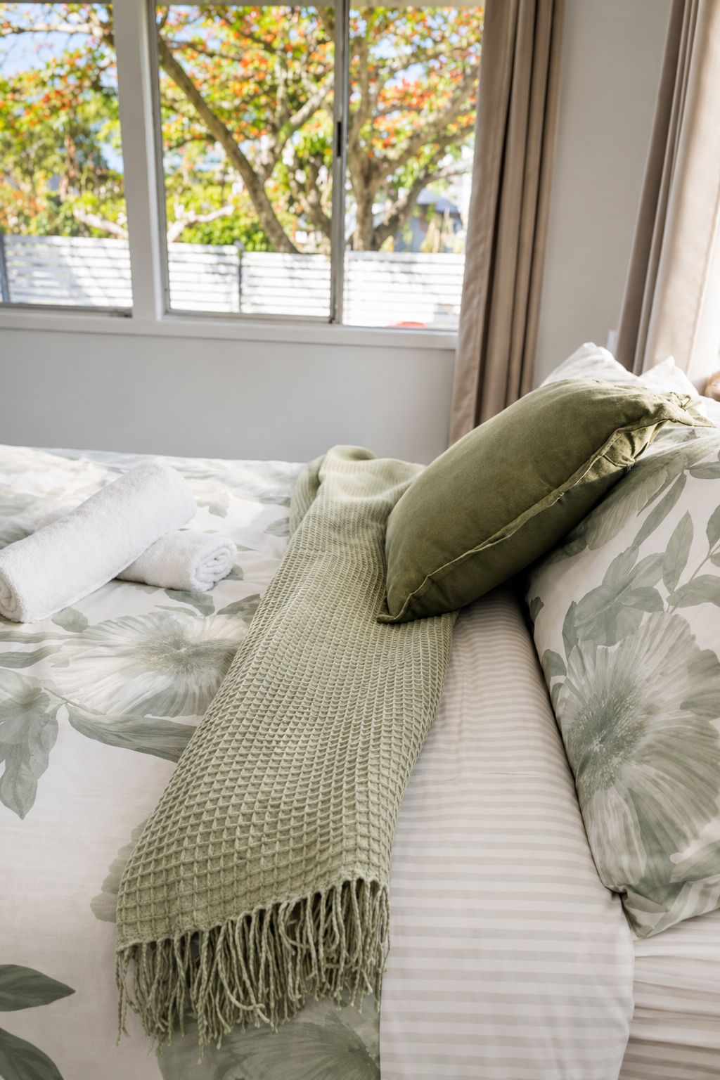 Un lit avec une couvre-lit à motifs floraux, un plaid vert en tricot et un coussin vert.