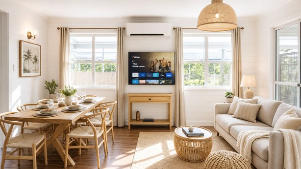 Ein modernes Wohnzimmer mit Essbereich, einer Couch, einem Fernseher und großen Fenstern.