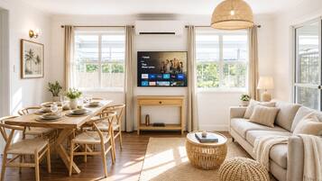 A modern living room with a dining area, a sofa, a TV, and large windows.