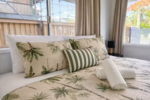 A bed with a floral-patterned bedspread, two pillows, a rolled towel, and a nightstand with a lamp. - Chic Urban Escape in Norman Park - Waterfront (Norman Park)