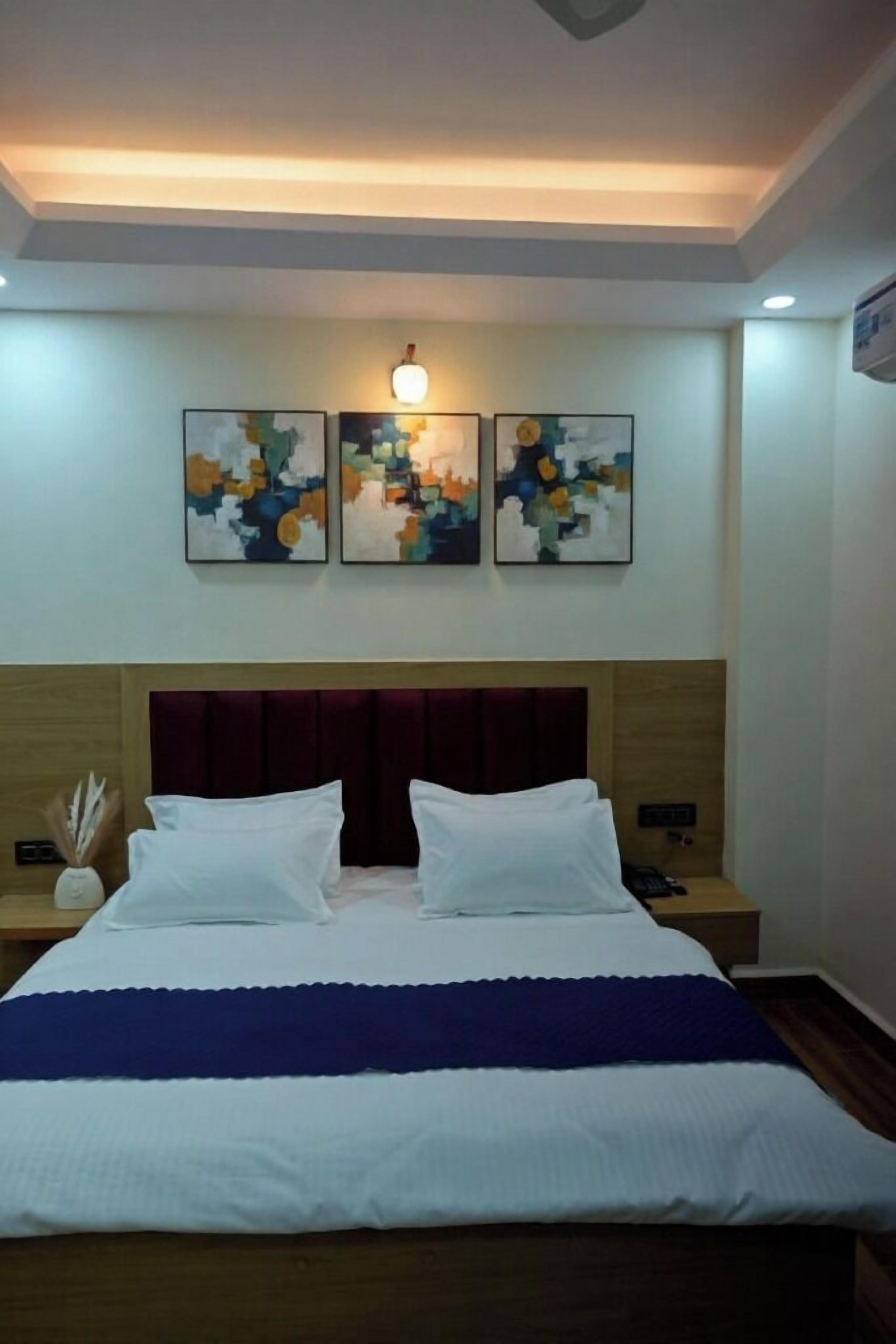 A hotel room with a large bed, two bedside tables, and three abstract paintings on the wall.