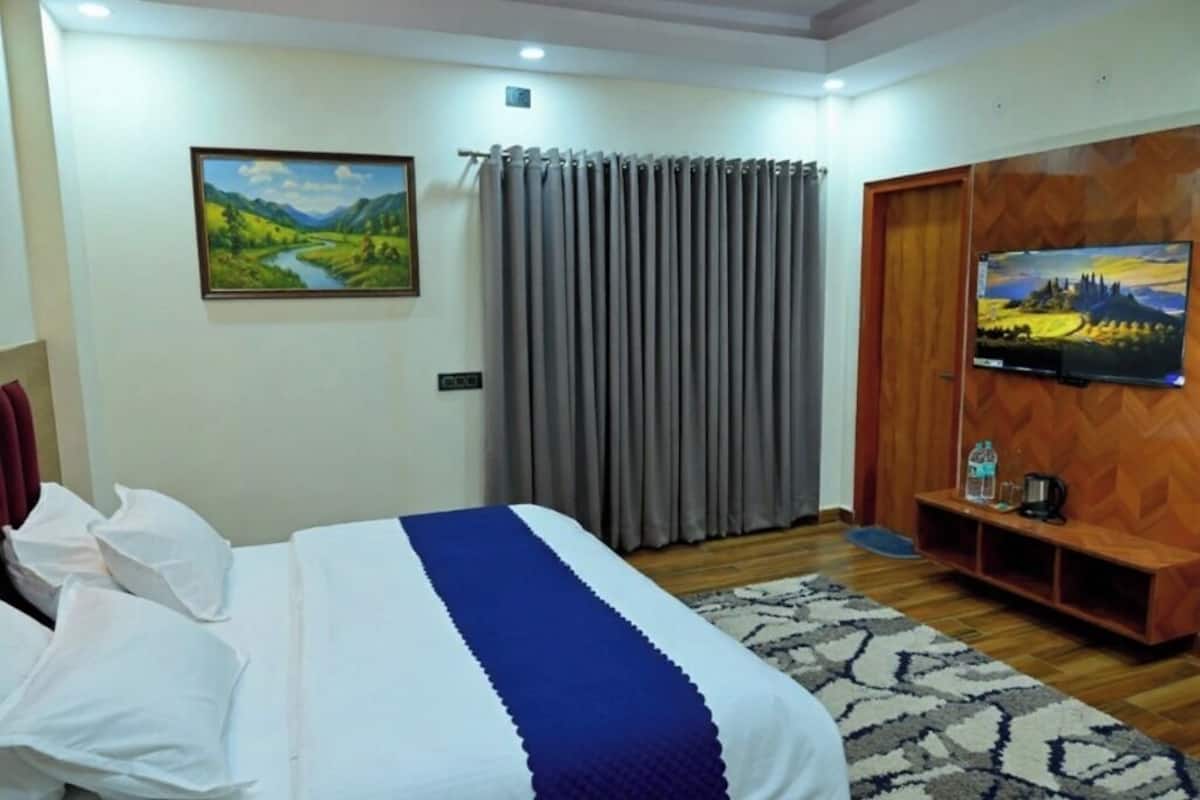 A hotel room with a bed, a TV, a wooden cabinet, and a painting on the wall.