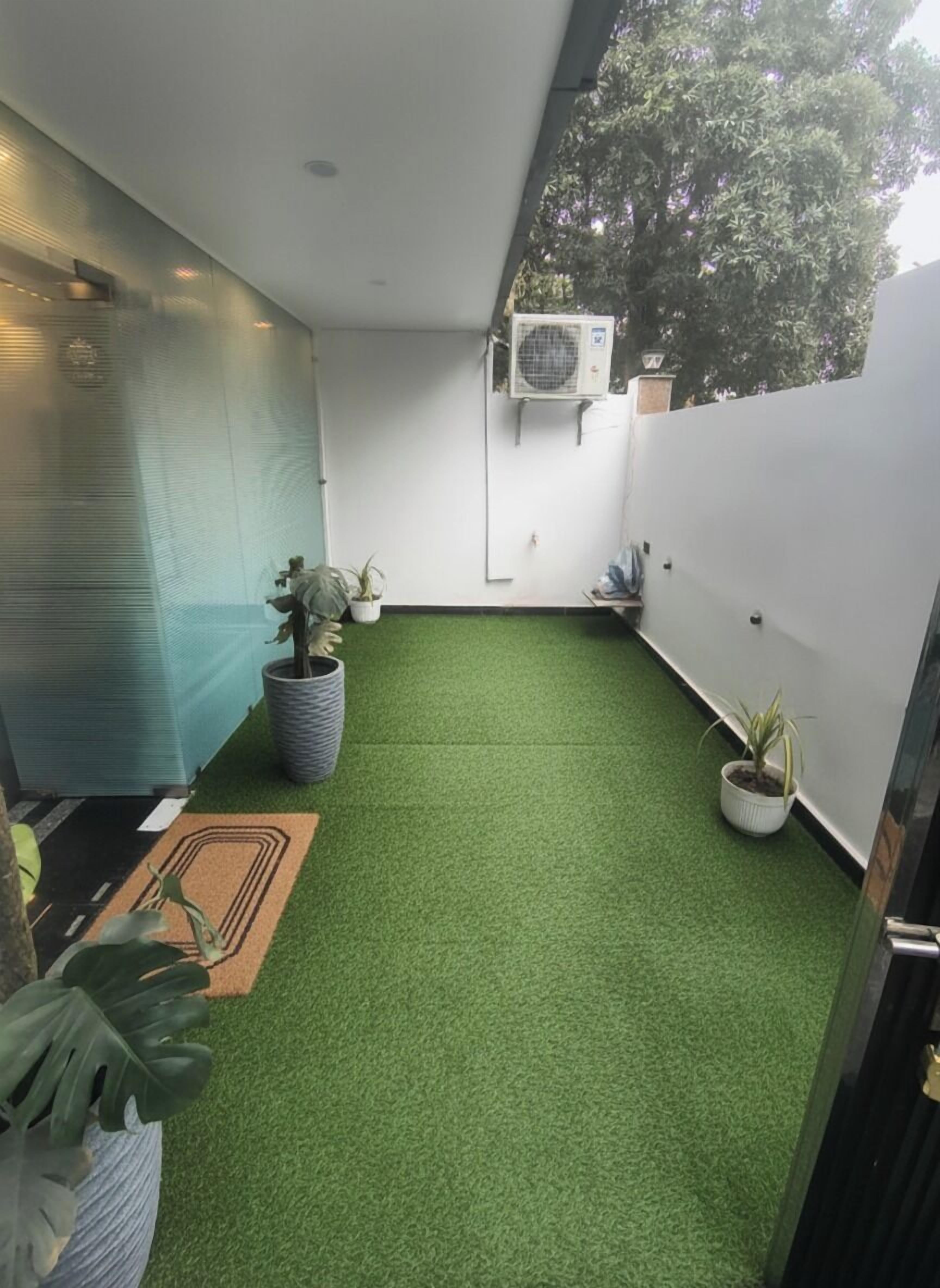 A narrow indoor space with artificial green turf, potted plants, and an air conditioning unit mounted on the wall.