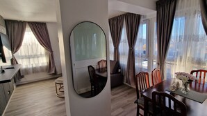 A modern hotel room with a flat-screen TV, a round mirror, a dining area with a table and chairs, and large windows with curtains. - Charming 2-bedroom Apartment in Central London (London)