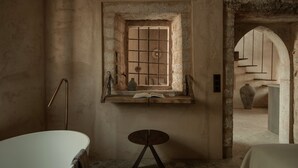 Une salle de bain rustique avec une baignoire, une petite table et une fenêtre à carreaux.