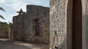 Un bâtiment en pierre avec une porte en bois, une fenêtre et une table avec des chaises à l’extérieur.