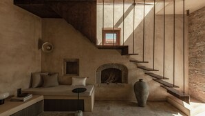 Une pièce chaleureuse avec une cheminée en pierre, un canapé et un escalier doté d’une rampe en bois.