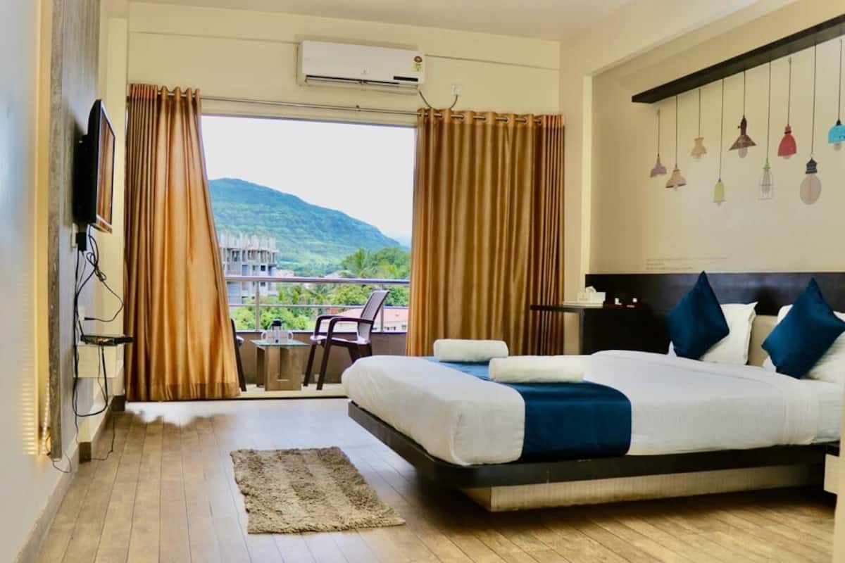 A hotel room with a large bed, a view of a mountain, and a balcony with a chair.