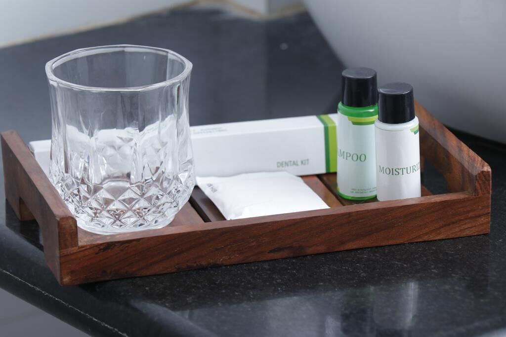 Una bandeja de madera con un vaso, un kit de higiene bucal y dos botellas de champú y crema hidratante.