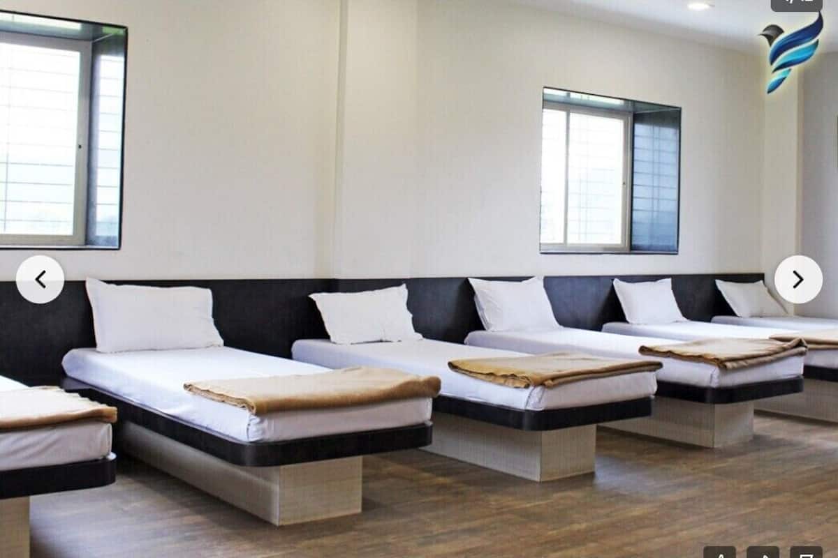 A hotel room with four single beds arranged in a row, each with a white mattress and a brown blanket.