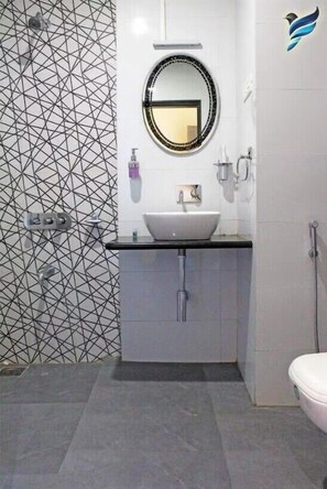 A modern bathroom with a geometric tile backsplash, a round mirror, a white sink, and a toilet. - Hotel Srushti Regency (Wai)