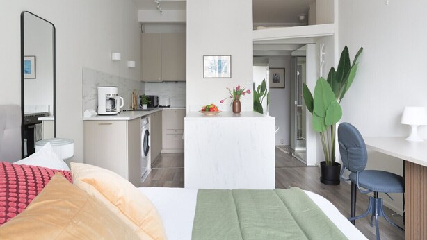 A modern hotel room with a bed, a desk, a chair, a small kitchenette, and a bathroom. - Stylish Studio in the Heart of Kallio (Helsinki)