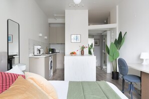 A modern hotel room with a bed, a desk, a chair, a small kitchenette, and a bathroom. - Stylish Studio in the Heart of Kallio (Helsinki)