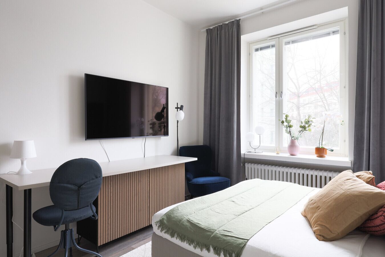Una habitación de hotel moderna con una cama, un escritorio con silla, un televisor y una ventana con cortinas.