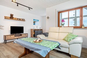 Un salon moderne avec un canapé, un téléviseur, un meuble de rangement en bois et une fenêtre donnant sur un beau paysage.