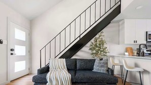 A modern living room with a dark grey sofa, a wooden coffee table with decorative balls, a striped throw blanket, and a staircase with a black railing. - Urban Oasis Loft Pet Yard Parking (Austin)