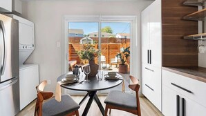 A modern kitchen with white cabinets, a stainless steel refrigerator, and a dining area with a round table and chairs. - Urban Oasis Loft Pet Yard Parking (Austin)