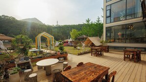A wooden deck with tables and chairs, a thatched-roof structure, and a modern building with large windows. - Harbor Diary Homestay (Xuancheng)
