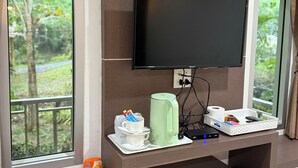 A hotel room with a flat-screen TV mounted on a wall, a coffee maker, a small refrigerator, and a window with a view of greenery. - Echo Samadhi (Ko Lanta)