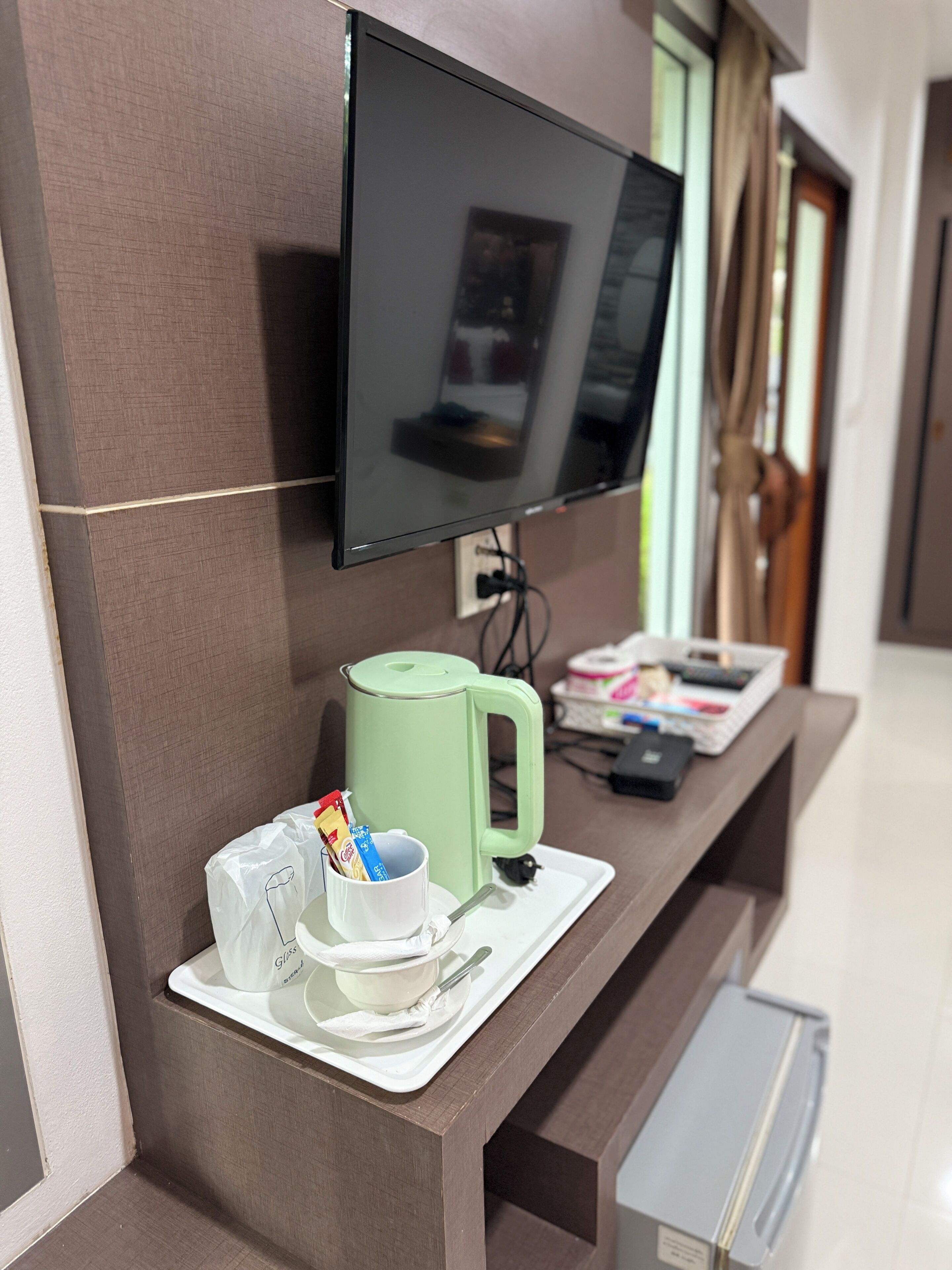 A modern hotel room with a flat-screen TV mounted on the wall, a coffee machine, and a tray with a mug and a cup of coffee.