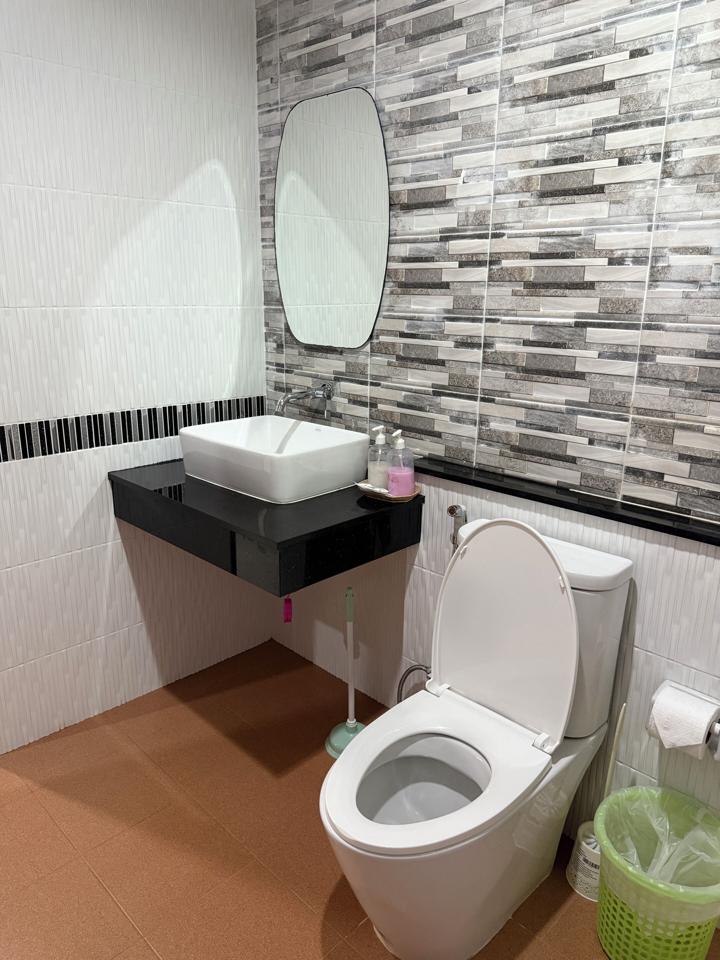 Une salle de bain avec un lavabo blanc, un plan de toilette noir et des toilettes.