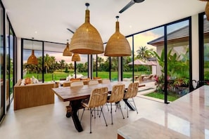 A modern dining area with a large table, wicker chairs, and pendant lighting. - Villa Samaddhi by BaliSuperHost (Bali)