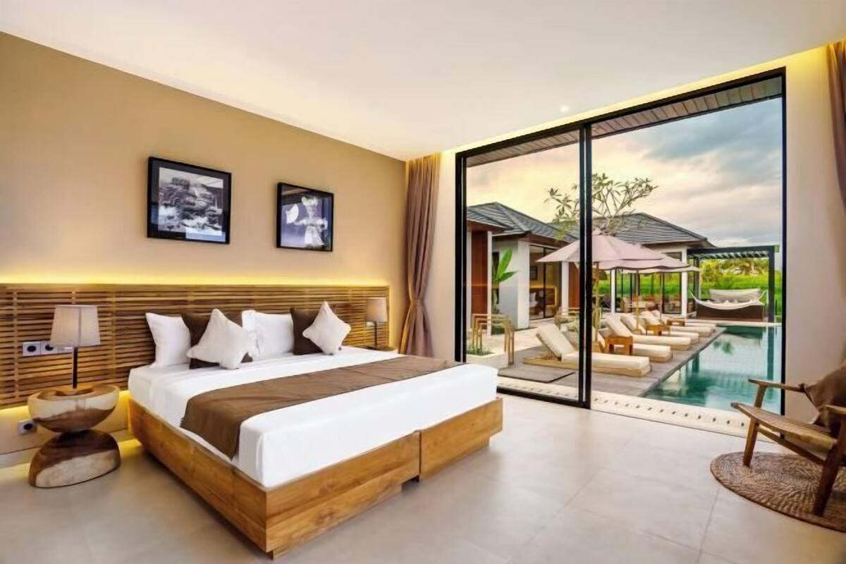 A modern hotel room with a large bed, a view of a pool, and a balcony.