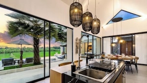 A modern kitchen with a large island, a dining area with a view, and a large window overlooking a garden. - Villa Lina by BaliSuperHost (Bali)
