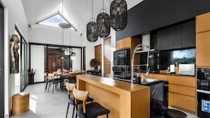 A modern kitchen with a central island, black pendant lights, and a dining area with chairs and tables. - Villa Lina by BaliSuperHost (Bali)