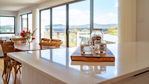 A kitchen with a large window, a wooden table, and a glass jar with water glasses on a tray. - Marmoris Bay of Fires - A laid back coastal retreat with shimmering ocean views (Binalong Bay)