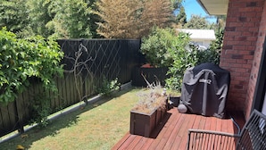 Una terraza de madera con una parrilla, una silla de mimbre y jardineras elevadas.