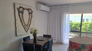 Un comedor con una mesa y sillas de madera, un florero con flores, una obra de arte colgada en la pared y una ventana con cortinas.