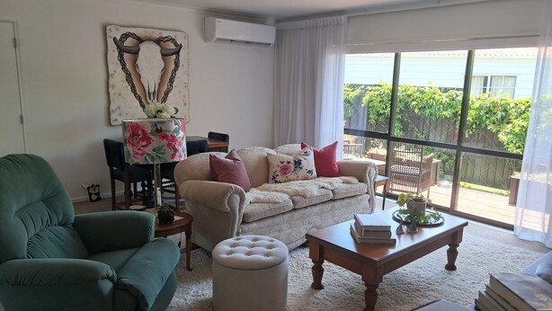 Un salón con sofá, reposapiés, mesa de centro y una silla. Hay un ventanal con vistas a zonas verdes.