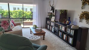 Una sala de estar con un sillón verde, una mesita de centro, una estantería y un ventanal con vistas al paisaje verde exterior.
