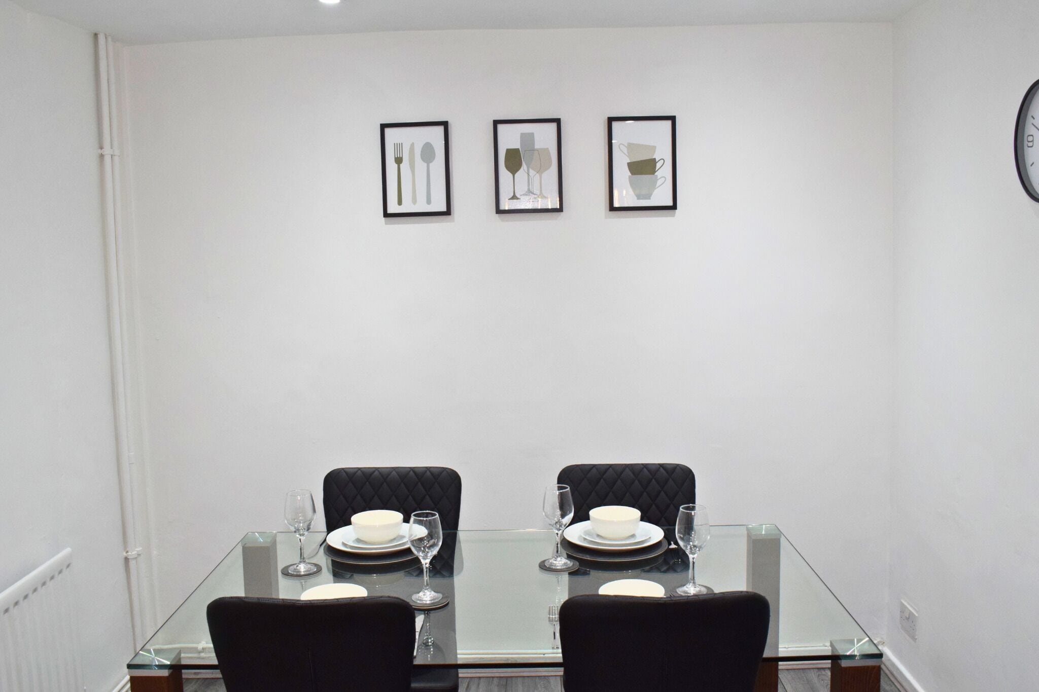 A dining area with a glass table, black upholstered chairs, and framed artwork on the wall.