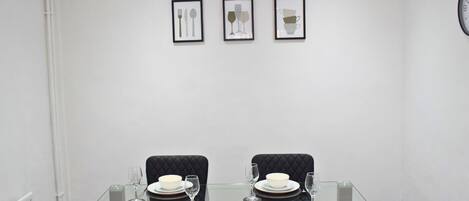 A dining area with a glass table, black upholstered chairs, and framed artwork on the wall.