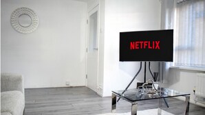 A modern living room with a glass coffee table, a flat-screen TV displaying 'NETFLIX', and a grey sofa. - Stylish 3-Bed House in Wolverhampton | Long Stays Welcome | Near Hospital (West Midlands)