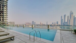 A rooftop swimming pool with a city skyline view, lounge chairs, and a modern building in the background. - Classic 2 Bedroom l Marina Views l Private Beach (Emaar Beachfront)