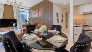 A modern dining area with a round table set for four, a city view, and a kitchen in the background. - Classic 2 Bedroom l Marina Views l Private Beach (Emaar Beachfront)