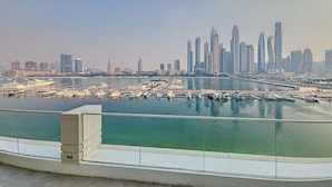 A marina with boats docked, a waterfront promenade, and a city skyline with high-rise buildings in the background. - Classic 2 Bedroom l Marina Views l Private Beach (Emaar Beachfront)